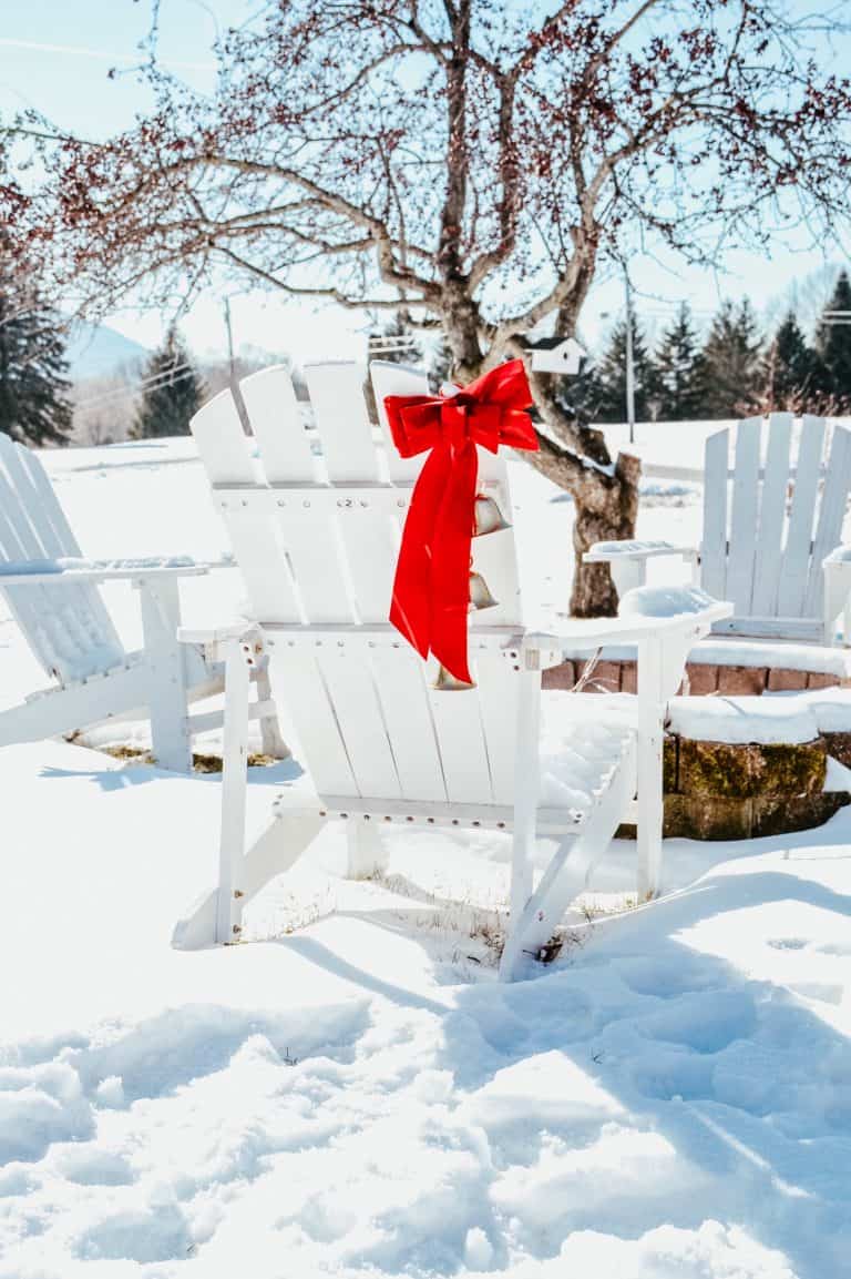 Adirondack chairs with a red bow in snow.
