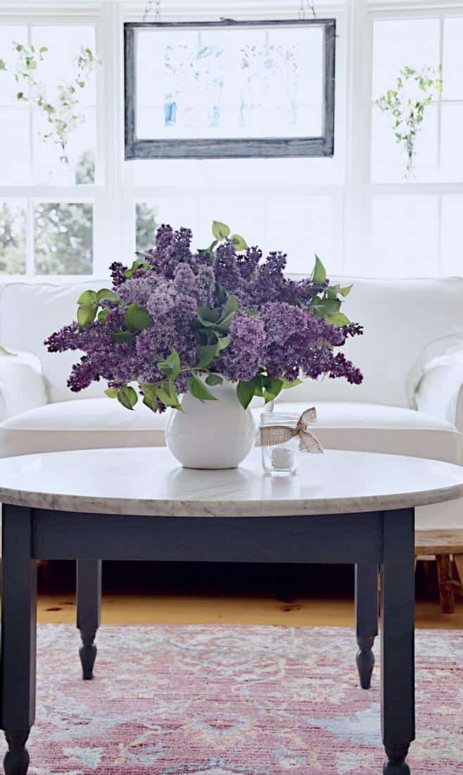 Sunroom makeover with white loveseat and lilacs on coffee table.