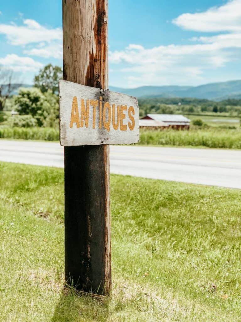A vintage sign that says antiques on a pole in front of a field, ideal for home decor enthusiasts and decorating lovers.