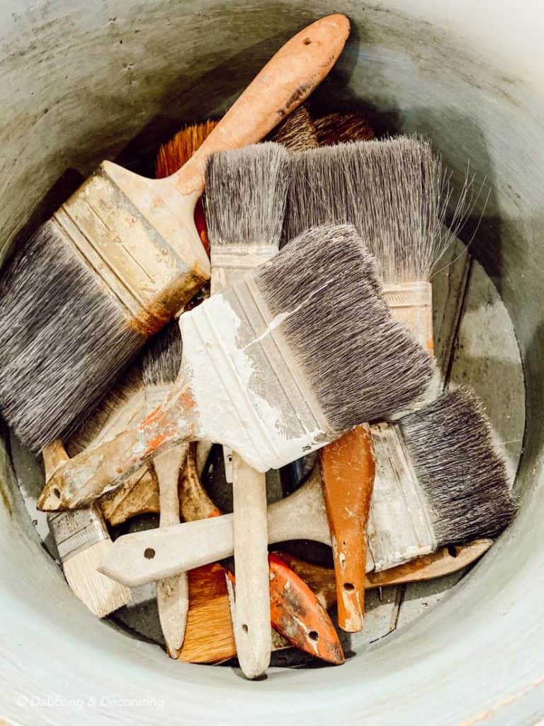 Vintage paint brushes in a decorative bucket for home decor.