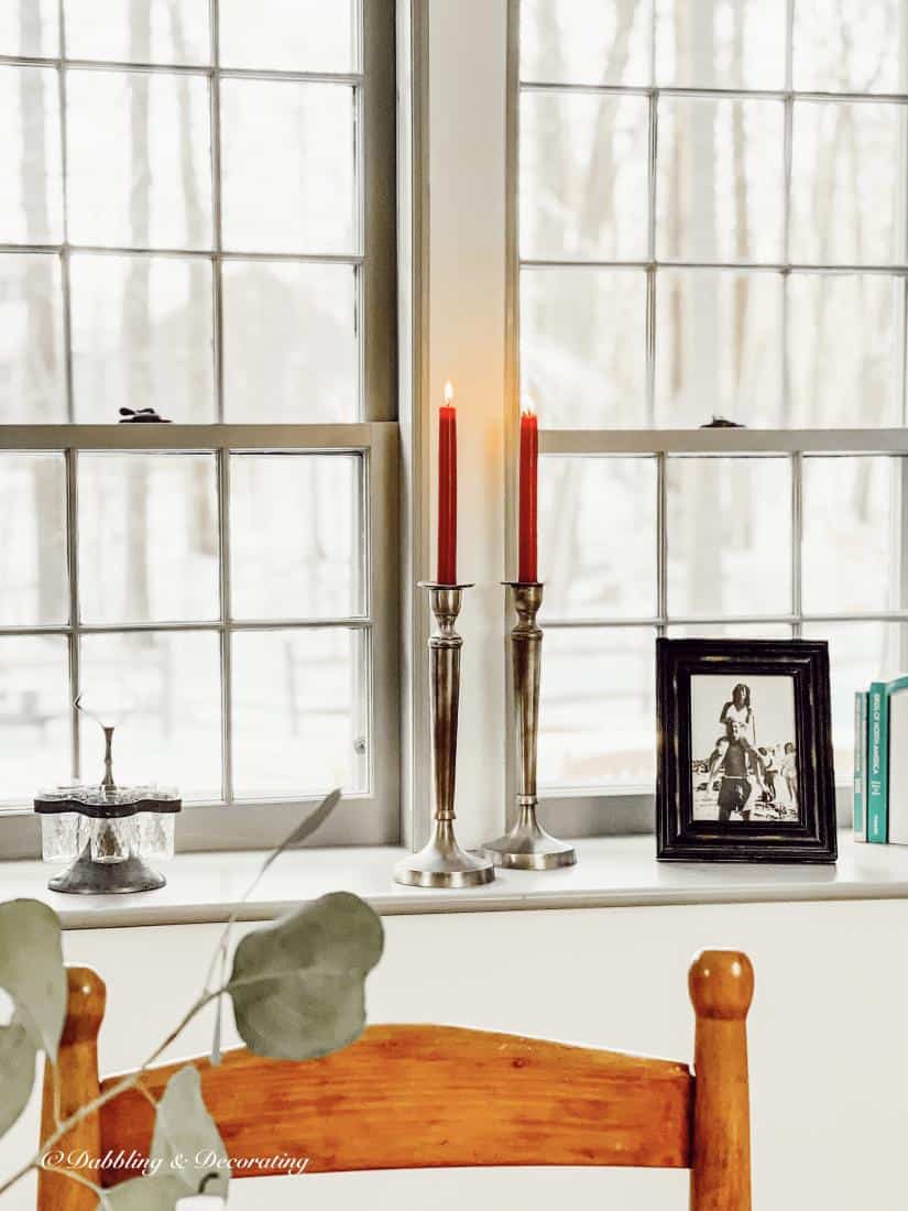 Two red tapered candles in pewter candlesticks on window sill with framed photo.