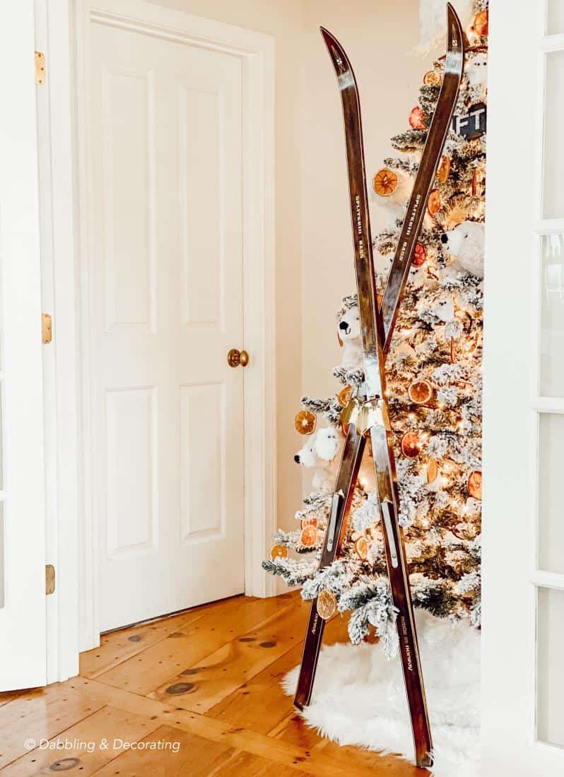 Wooden vintage skis crossed leaning up against Christmas tree in corner with white polar bears, and DIY orange ornaments.