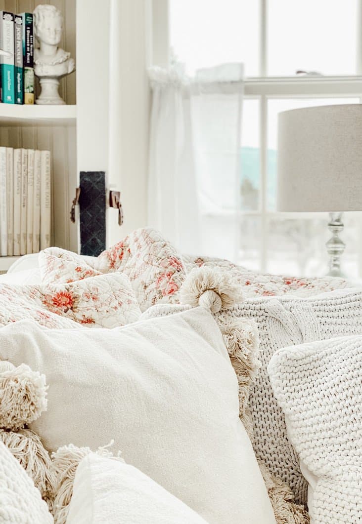 Cozy piles of pillows on white sectional couch in small home library.