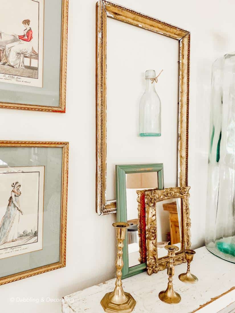 Gold frames layered on wall with bottles, mirrors, and brass candlesticks.