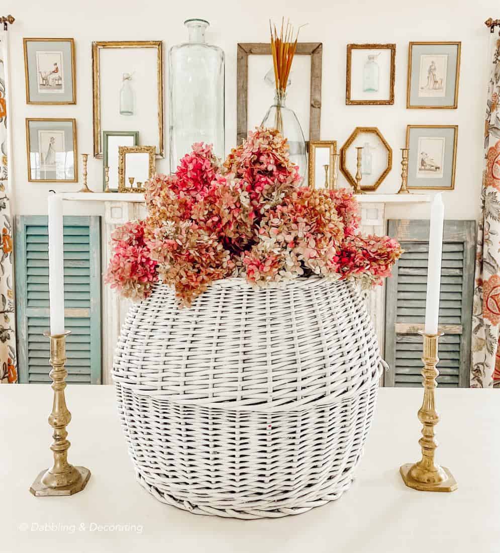 Large white basket with hydrangeas and brass candlestick centerpiece in dining room.