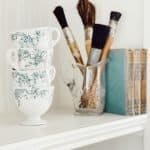 teacups, paintbrushes, and books on a bookshelf