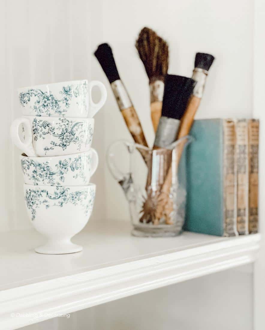 teacups, paintbrushes, and books on a bookshelf