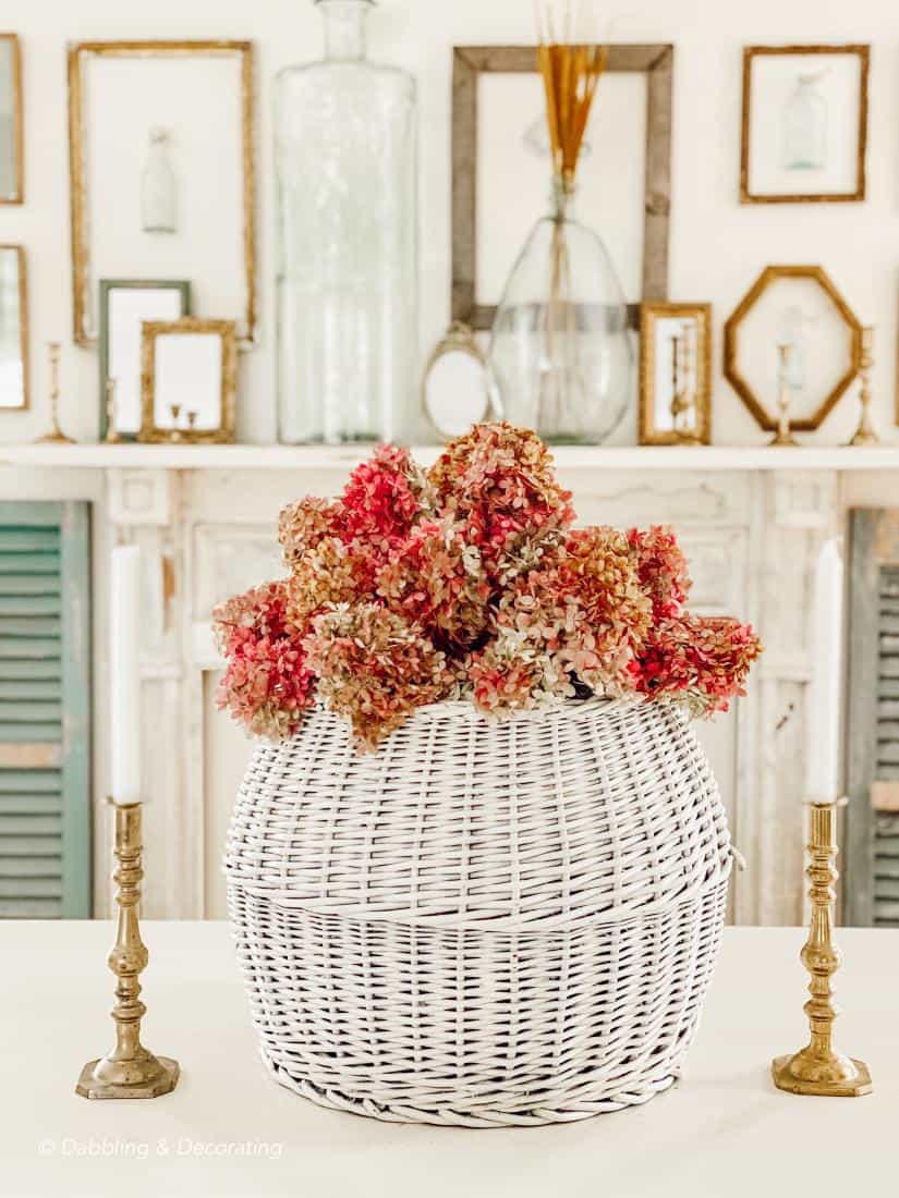 Fall hydrangeas centerpiece in large white basket in front of mantel wall display.