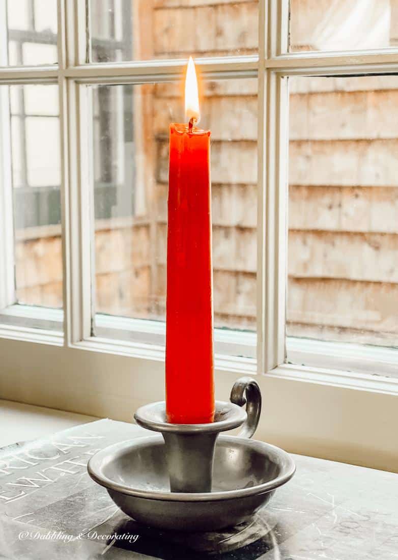 Lit red candle and pewter candlestick on vintage book on window sill