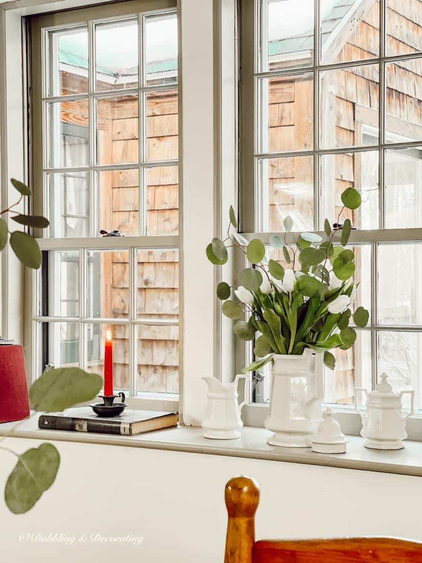 Window sill decor with white tea set and green and white flower display.