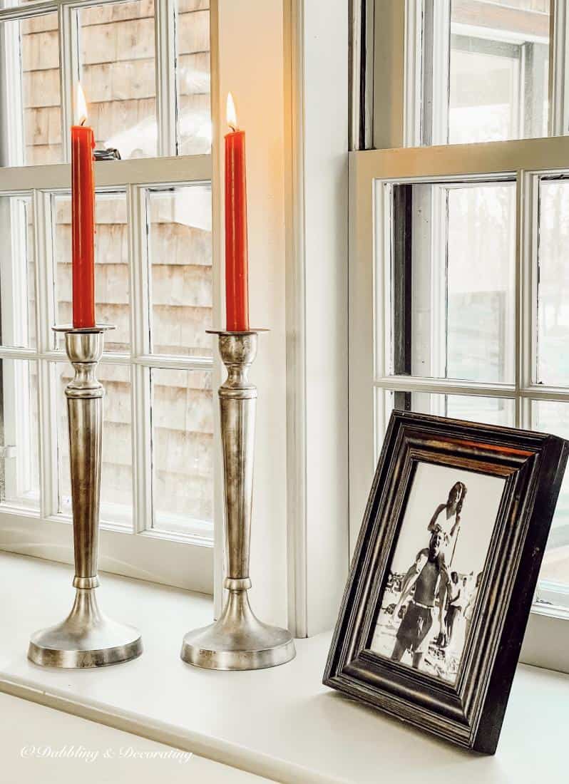 Pewter candlesticks with red tapered candles and framed photograph on window sill.