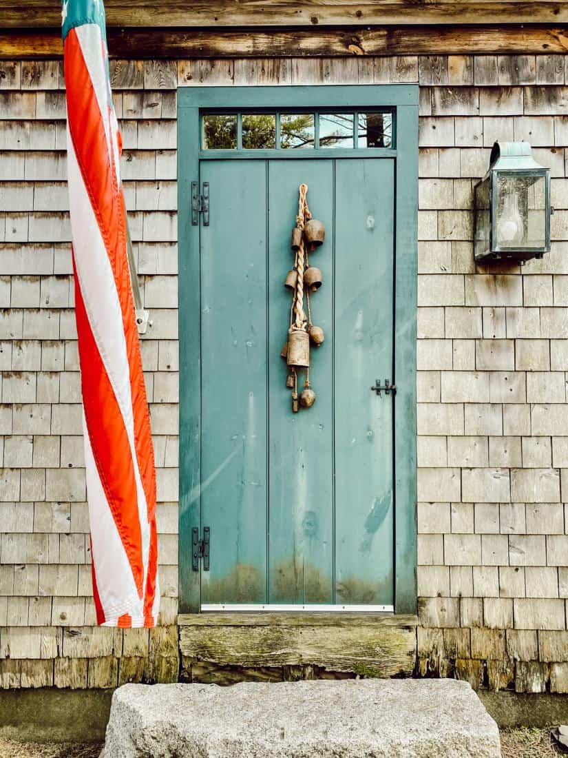 An old front door with weathered cedar shake siding on a house with flag.