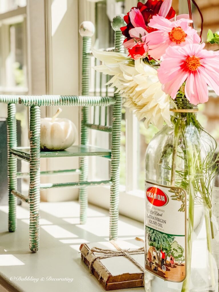 Window sill decor ideas with small doll chairs and a vintage bottle with fall flowers, books, and white pumpkin on ledge.