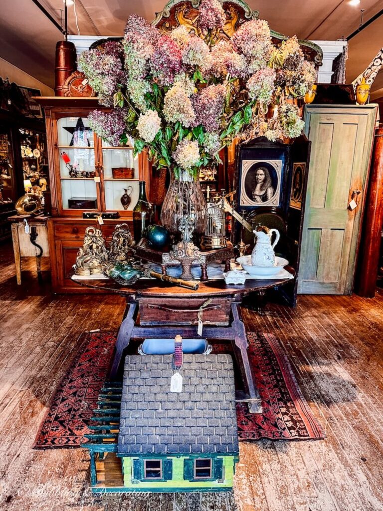Entryway to Windham Antique Center in Bellows Falls, Vermont with oversized vase filled with fall hydrangeas on table along with antiques.