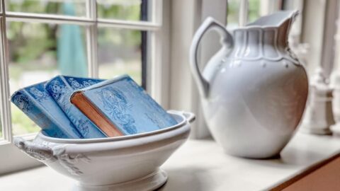 Windowsill decor with ironstone and vintage blue books in a bowl.