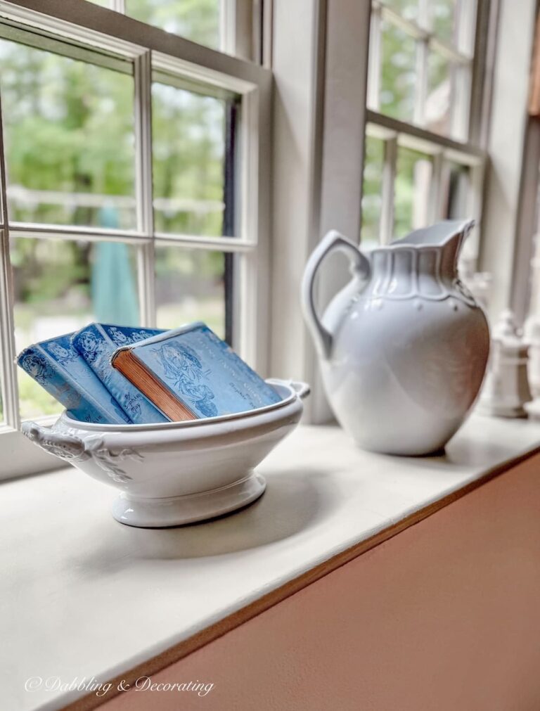 Windowsill decor with ironstone and vintage blue books in a bowl.