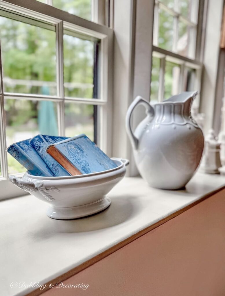 Windowsill decor with ironstone and vintage blue books in a bowl.