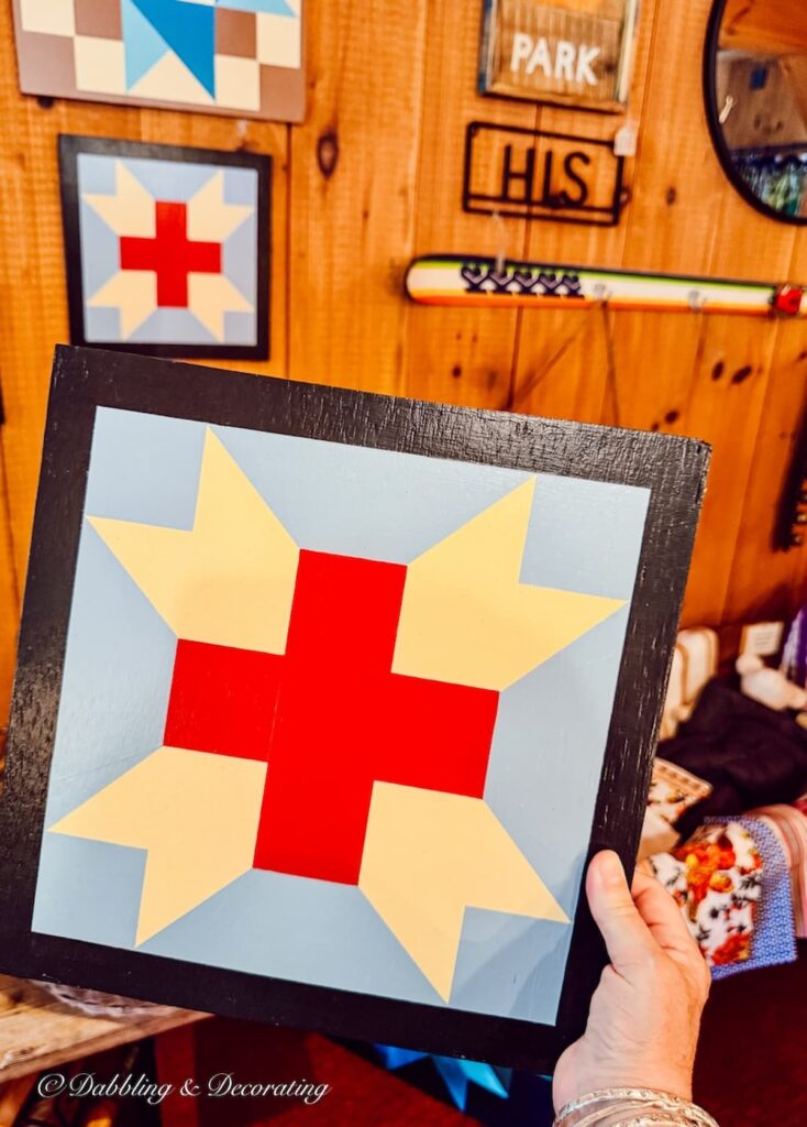 Barn Quilt with red cross and light blue colors framed in vintage shop.