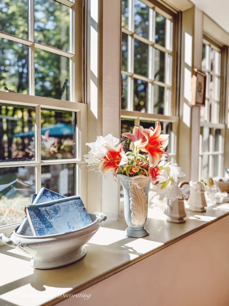Vintage blue vase with colorful pink flowers in long cozy windowsill decor with ironstone accessories and vintage blue books.