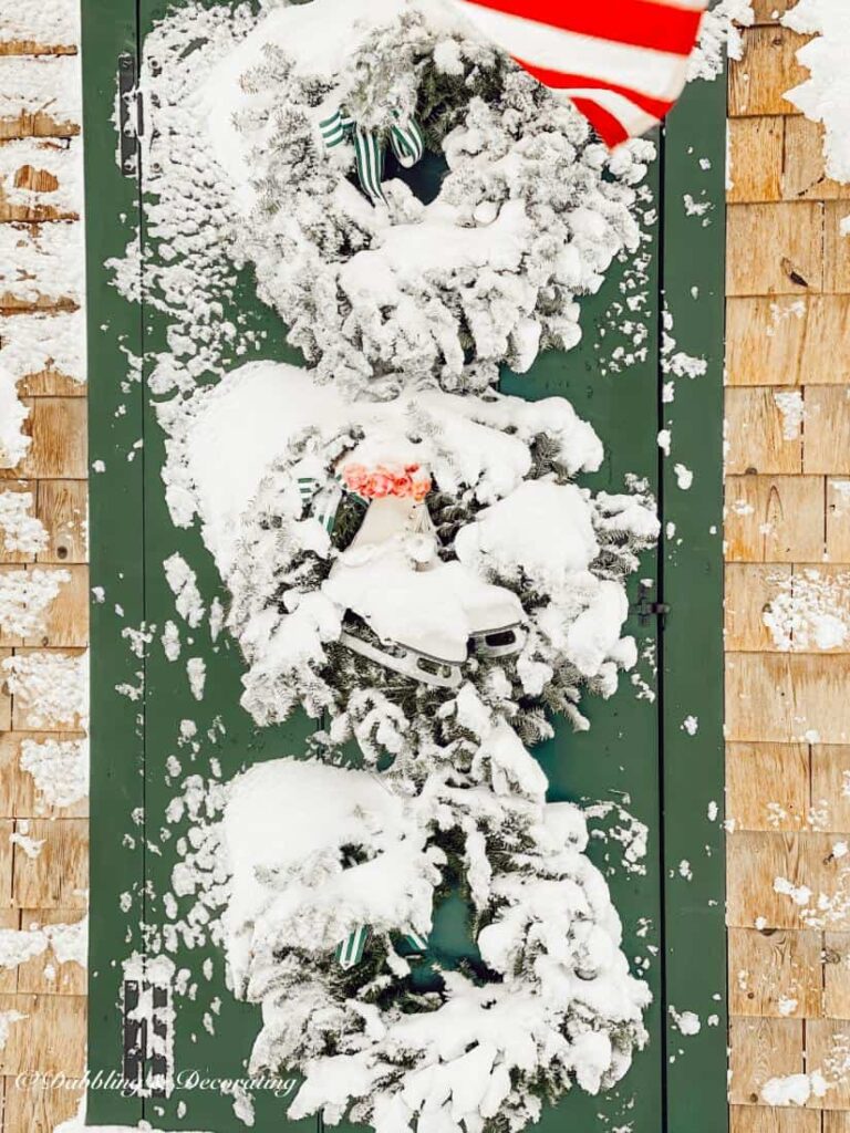 Three Snowy wreaths on front door with vintage ice skates and pink flowers.