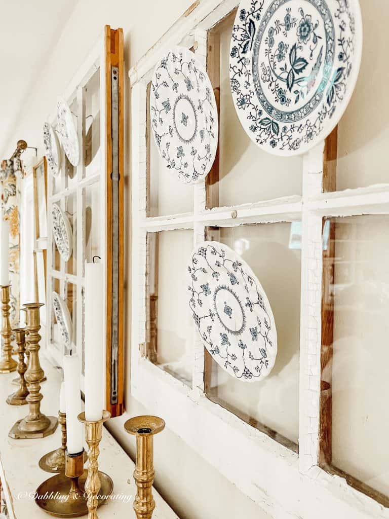 Salvaged windows with vintage small plates and brass candlestick DIY over mantel.