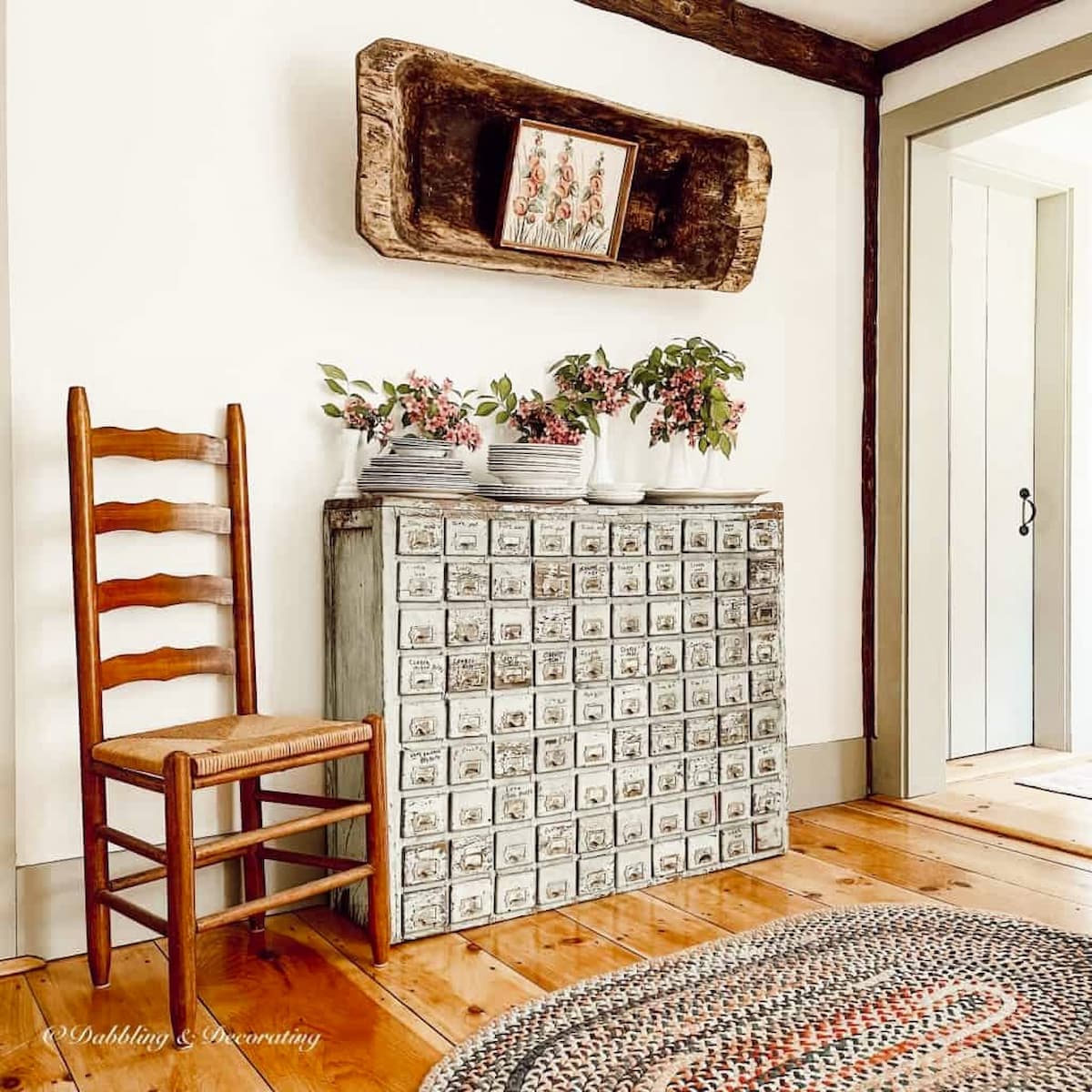 Vintage apothecary cabinet with 90 small drawers decorated with pink flowers, a chair and handmade braided rug in vintage home.