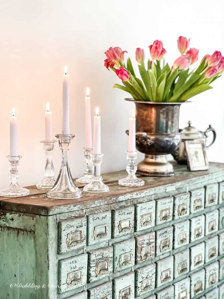 Apothecary vintage cabinet decorated with flowers and candlesticks.