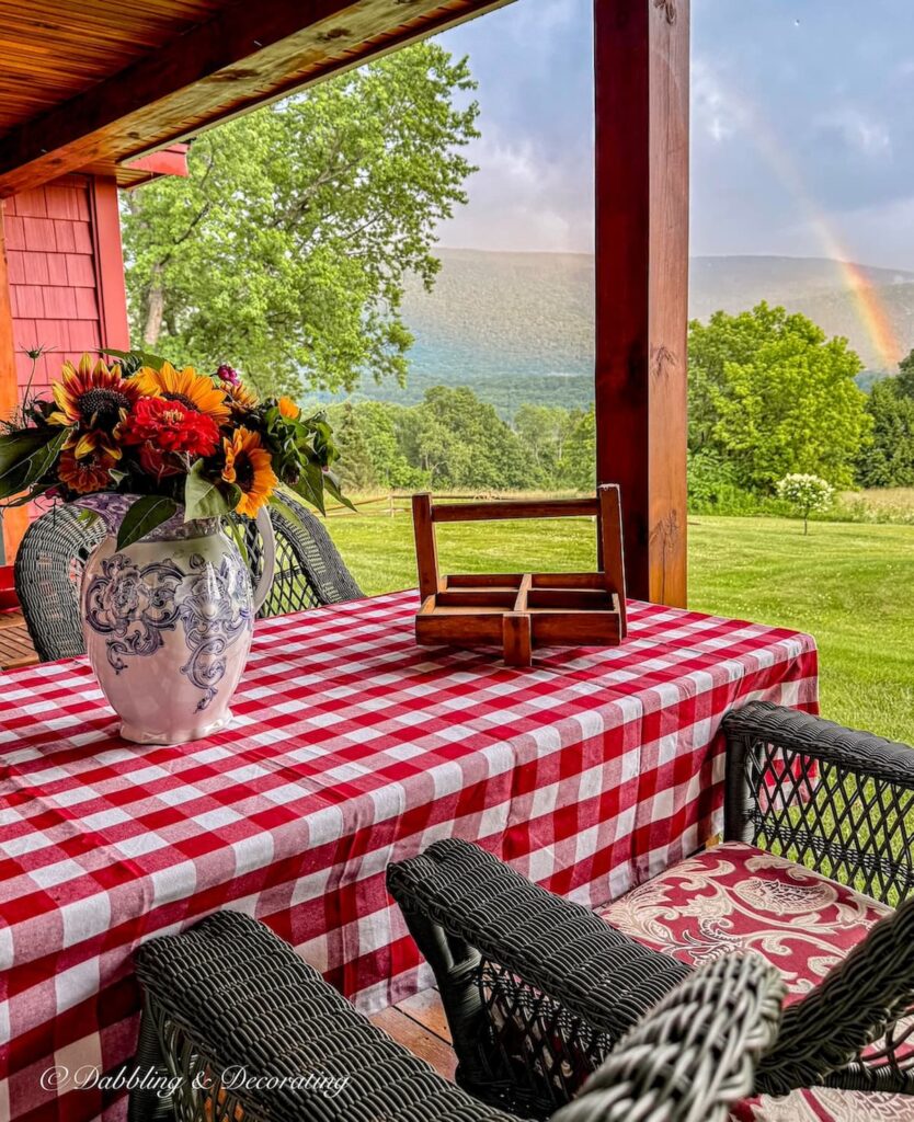 Outdoor porch table with red gingham table cloth, summer flower bouquet and rainbow with mountain views from Vermont porch.