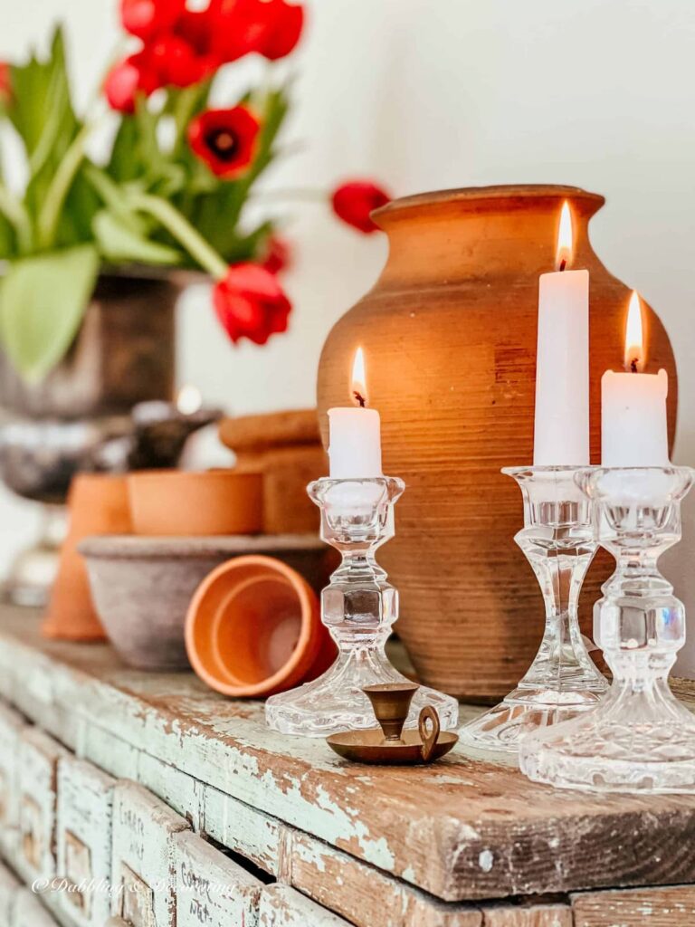 Decorative terracotta pots indoors on an apothecary cabinet with crystal candlesticks and red tulips for spring.
