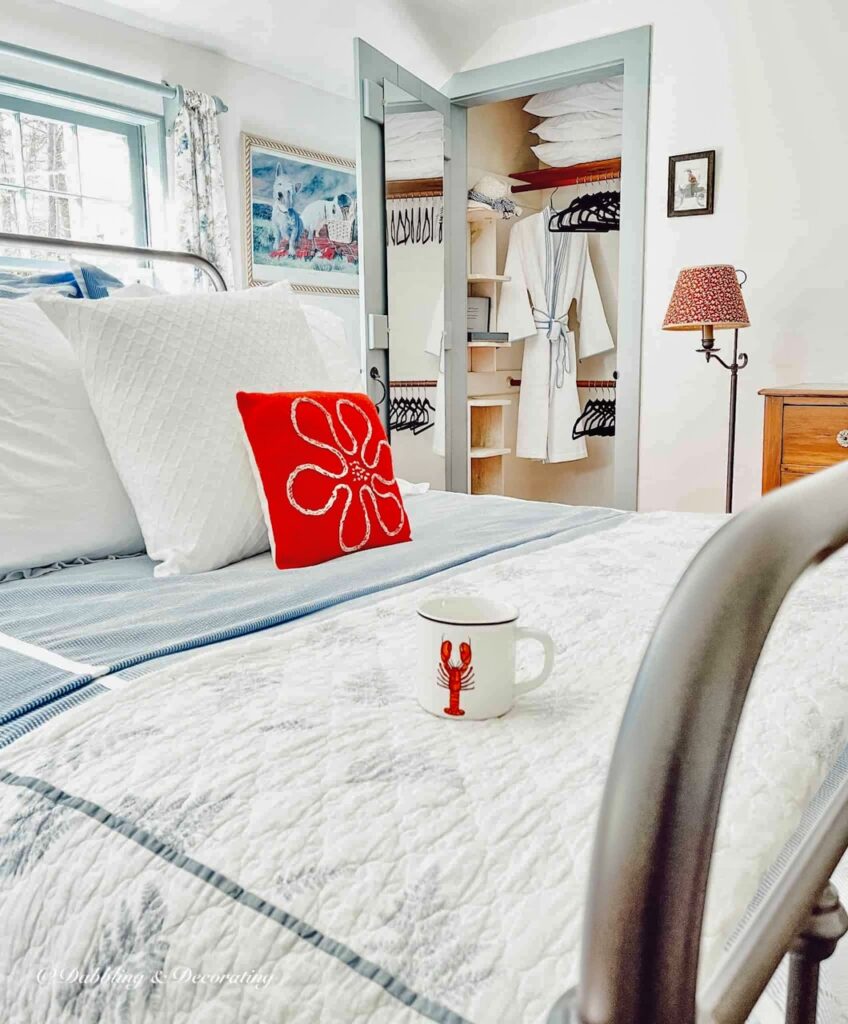 Small guest bedroom with wrought iron bed in front of open closet with bathrobe and black velvet clothes hangers.