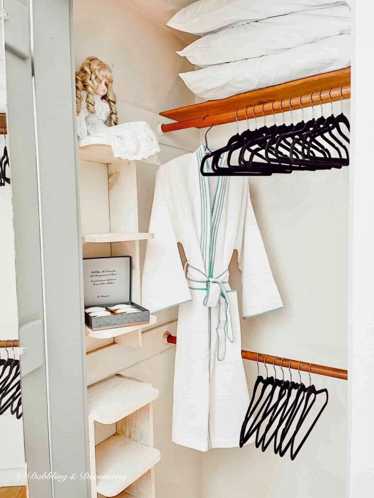 Small closet with velvet black clothes hangers, hanging white bathrobe and luxury soaps.
