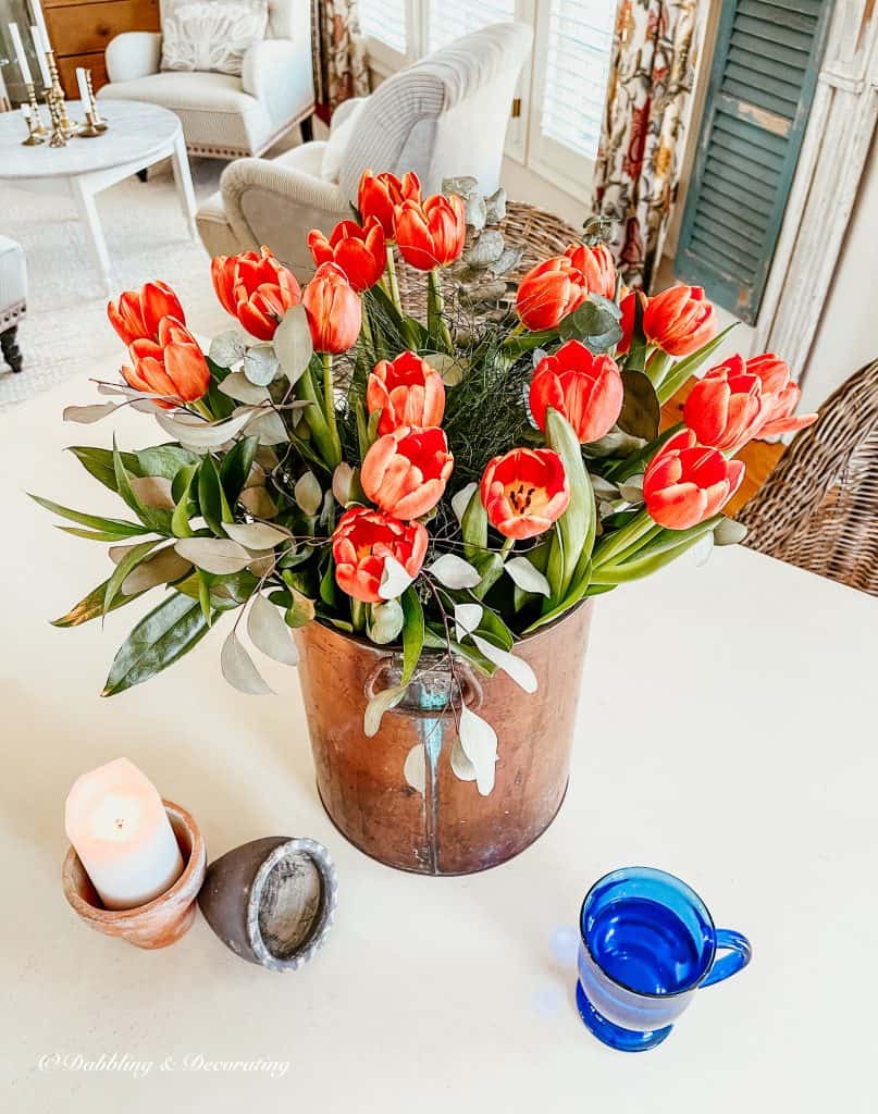 Bouquet of orange tulips in a copper bucket on the table.