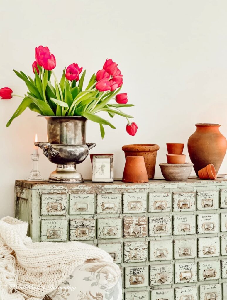 Antique apothecary styled with terracotta pots indoors with a vintage silver champagne bucket filled with pink tulips.