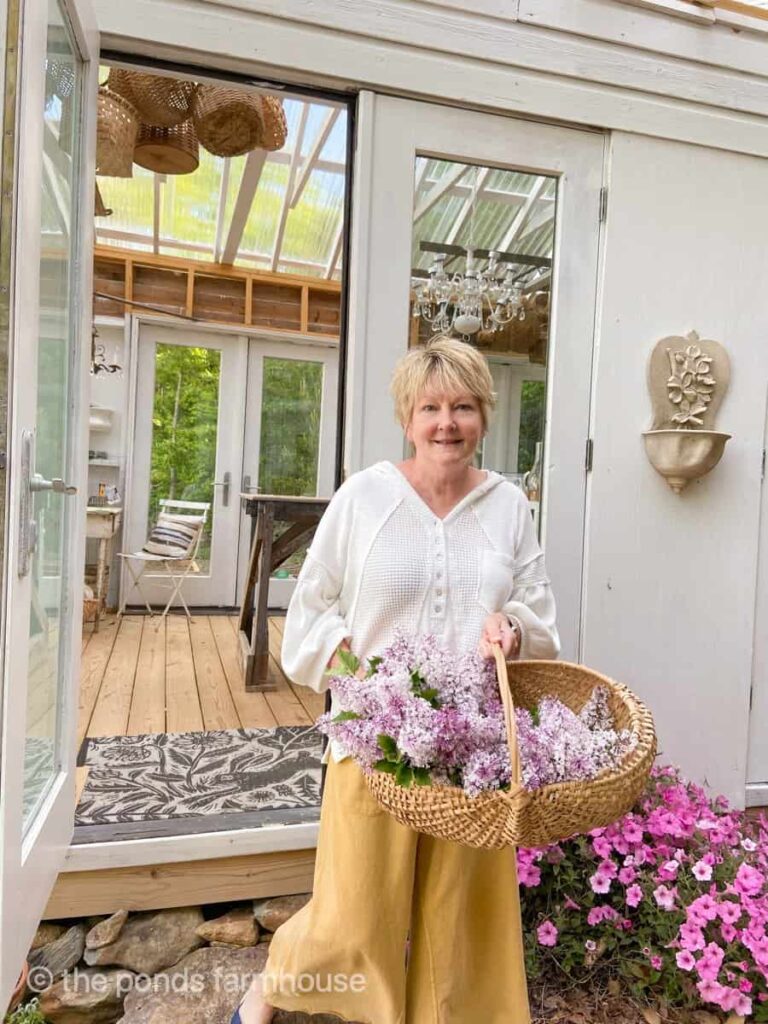 Woman with basket of lilacs outside of a greenhouse.