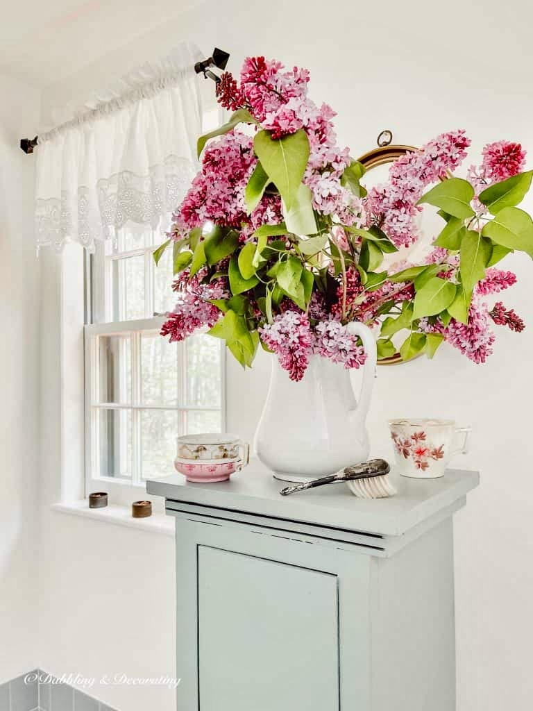 Purple Lilac bouquet in white pitcher in bathroom.