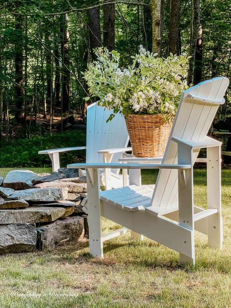 Two white Adirondack chairs with a large basket filled with white and green wild flowers around stone fire pit. Front porch flower pots ideas for spring and summer.