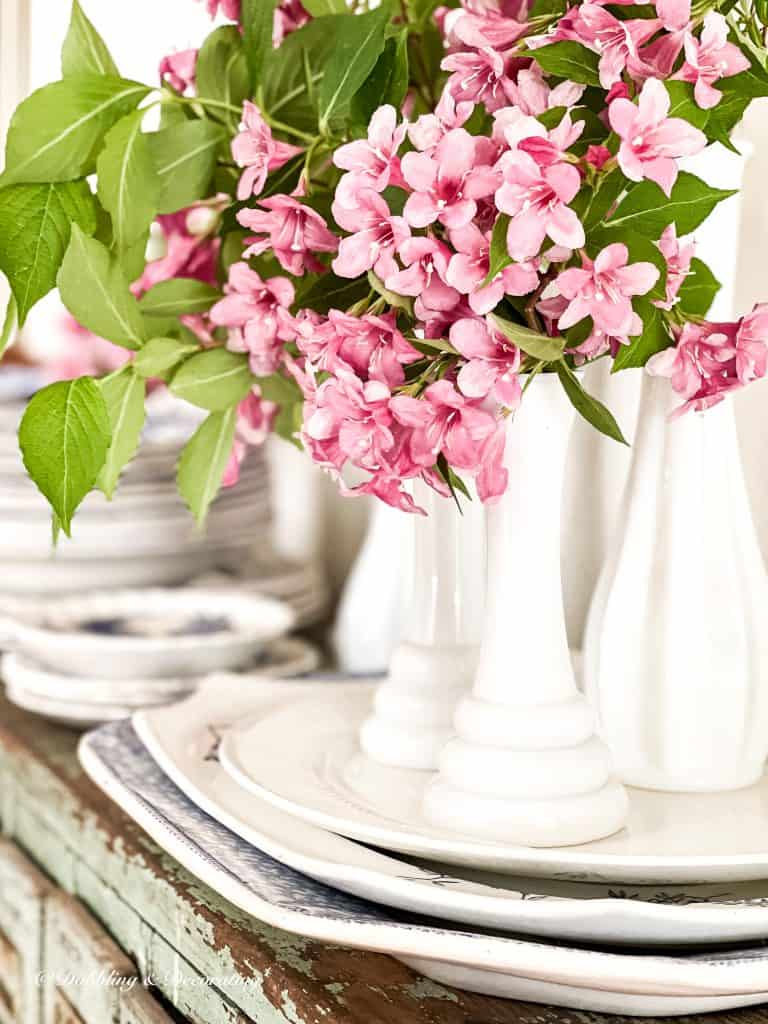 5 Clever Ways to Decorate with Yard Sale Finds.  Milk glass bud vases with pink flowers and dishes.