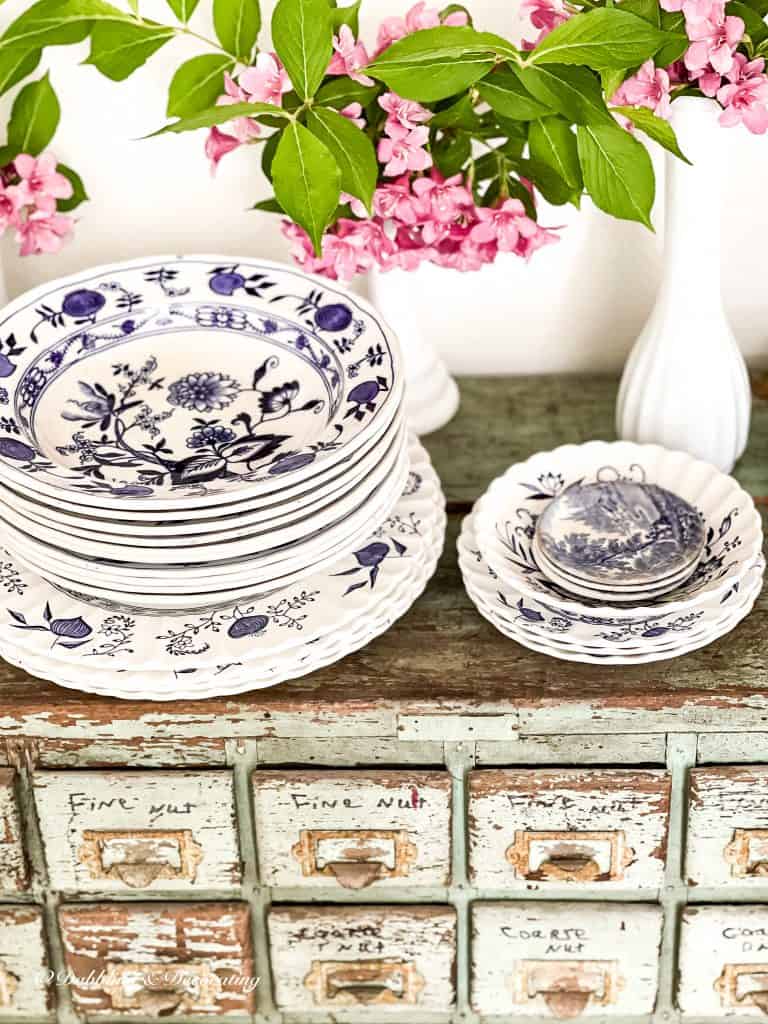 5 Clever Ways to Decorate with Yard Sale Finds.  Stack of blue and white dishes and pink flowers.