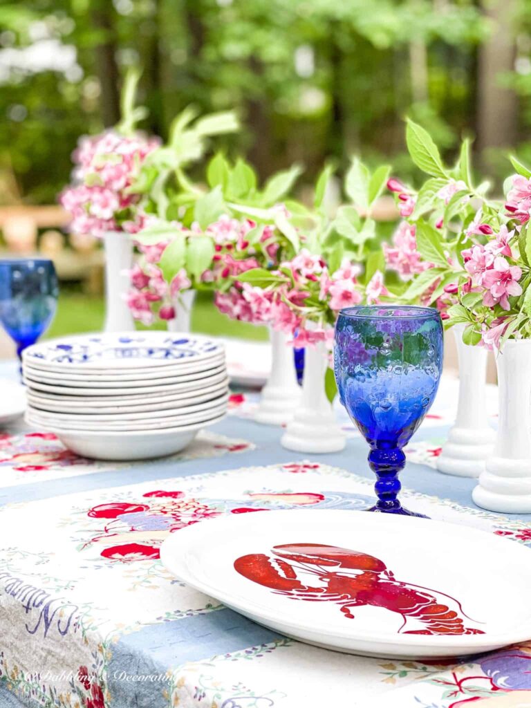 Outdoor summer tablescape with milk glass vases, pink flowers, lobster plates and blue and vintage details.