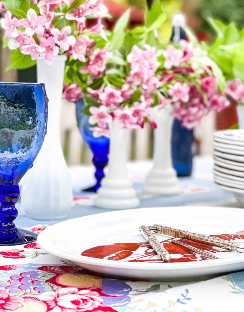 Outdoor summer tablescape with milk glass vases and vintage dishware.