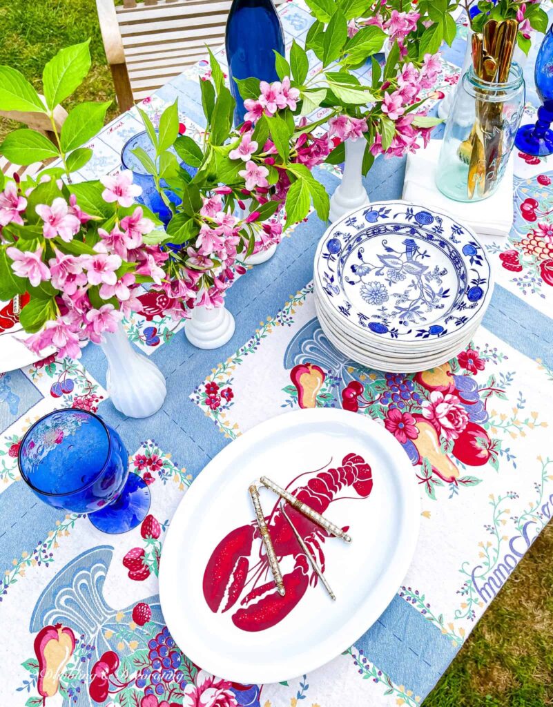 Outdoor summer tablescape with vintage finds: milk glass vases, blue and white dishes and vintage blue tablecloth.