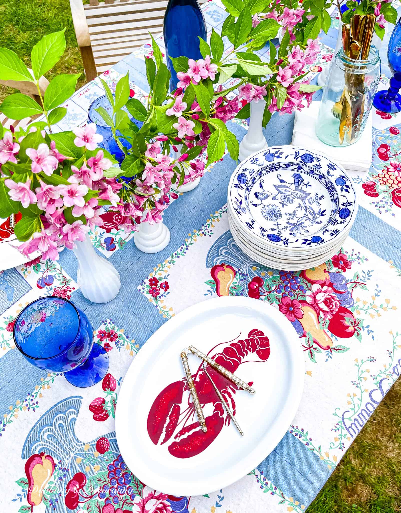 Outdoor summer tablescape with vintage finds: milk glass vases, blue and white dishes and vintage blue tablecloth.