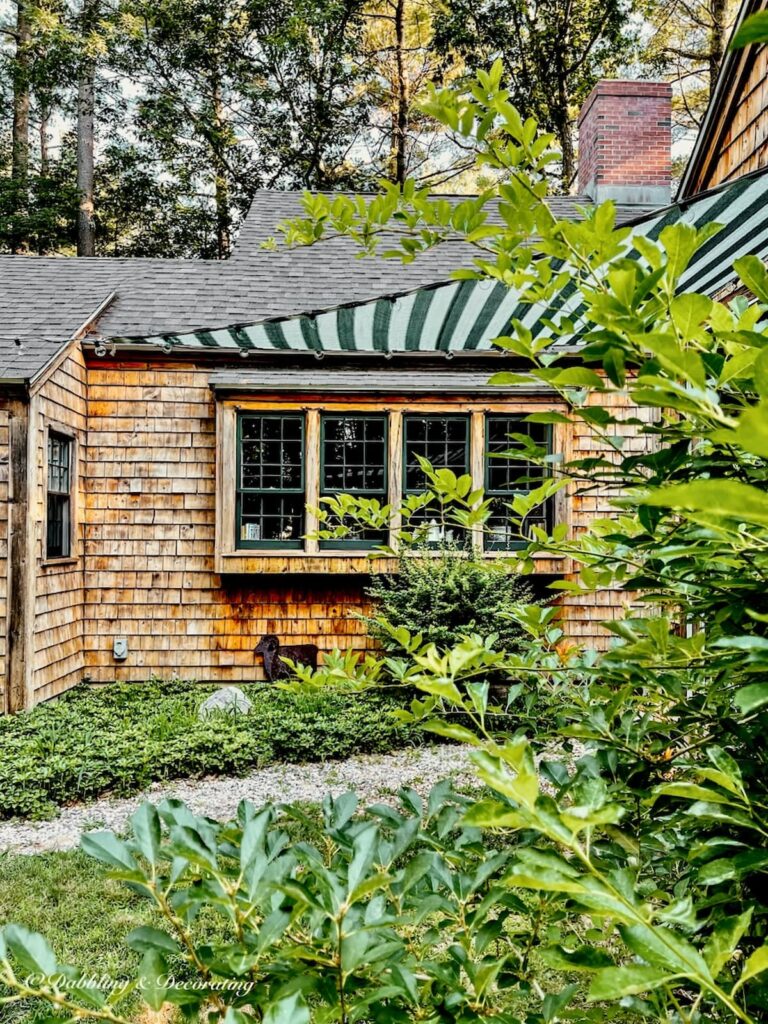 Cedar Shakes home with green and white striped sun shade triangle awning with lights over walkway.