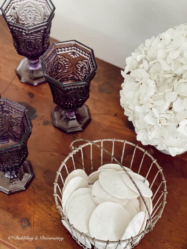 antique amethyst glassware presented on dark wood with white hydrangeas.