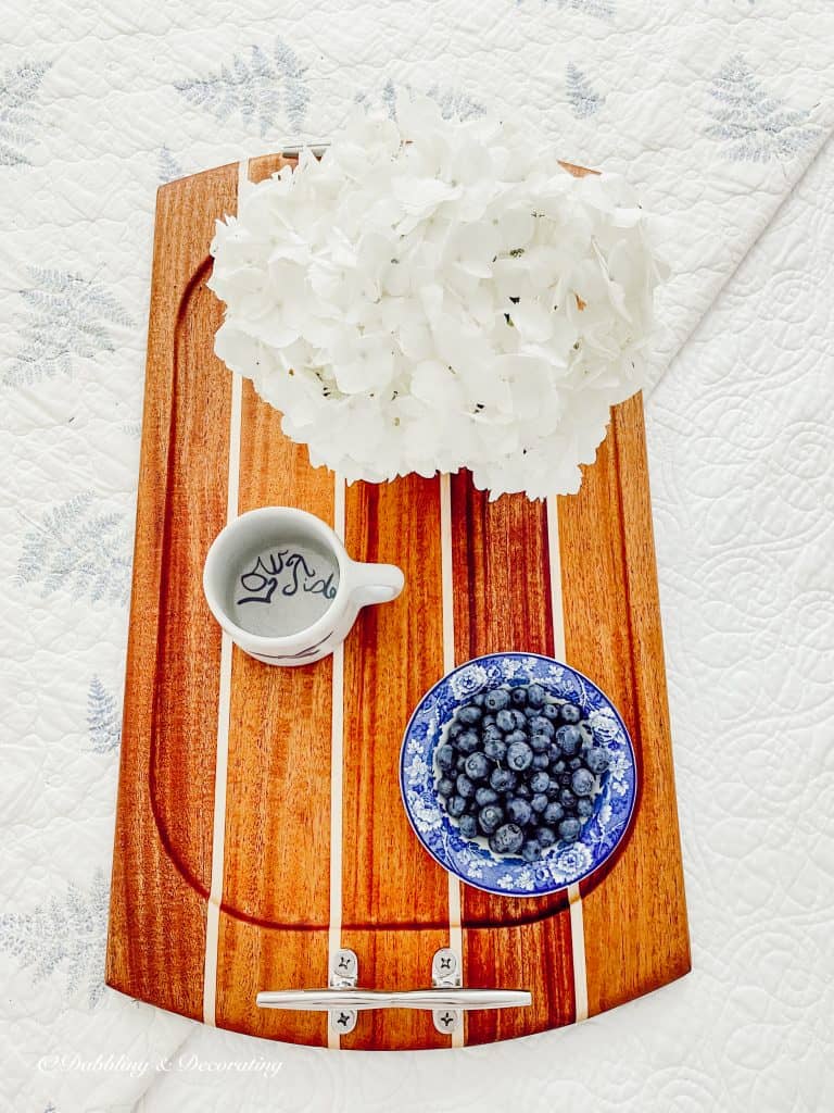 White hydrangeas with bowl of blueberries on bed with mug.