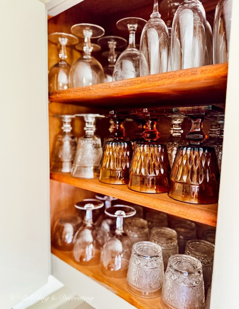 Open kitchen cabinet with vintage glassware organized.