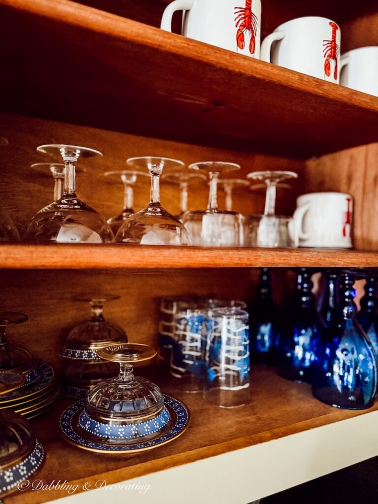 Shelving in kitchen with open cupboard door with vintage glassware organized