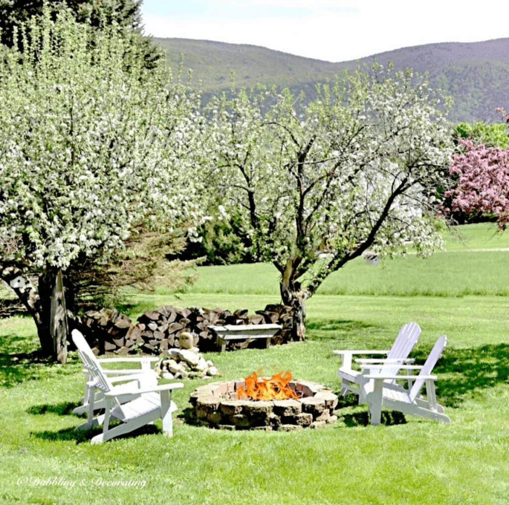 Backyard stone fire pit with Four Adirondack Chairs with Apple trees and mountain view.