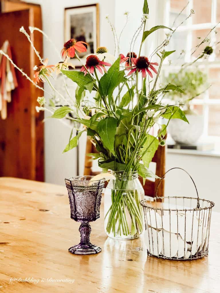 Antique amethyst glassware on table with flowers and basket of sand dollars.