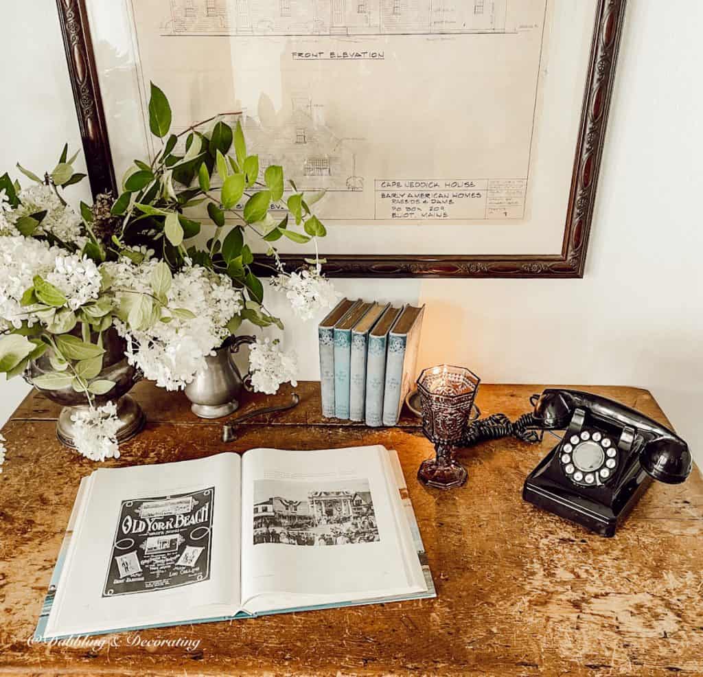 antique table with books, flowers, and telephone